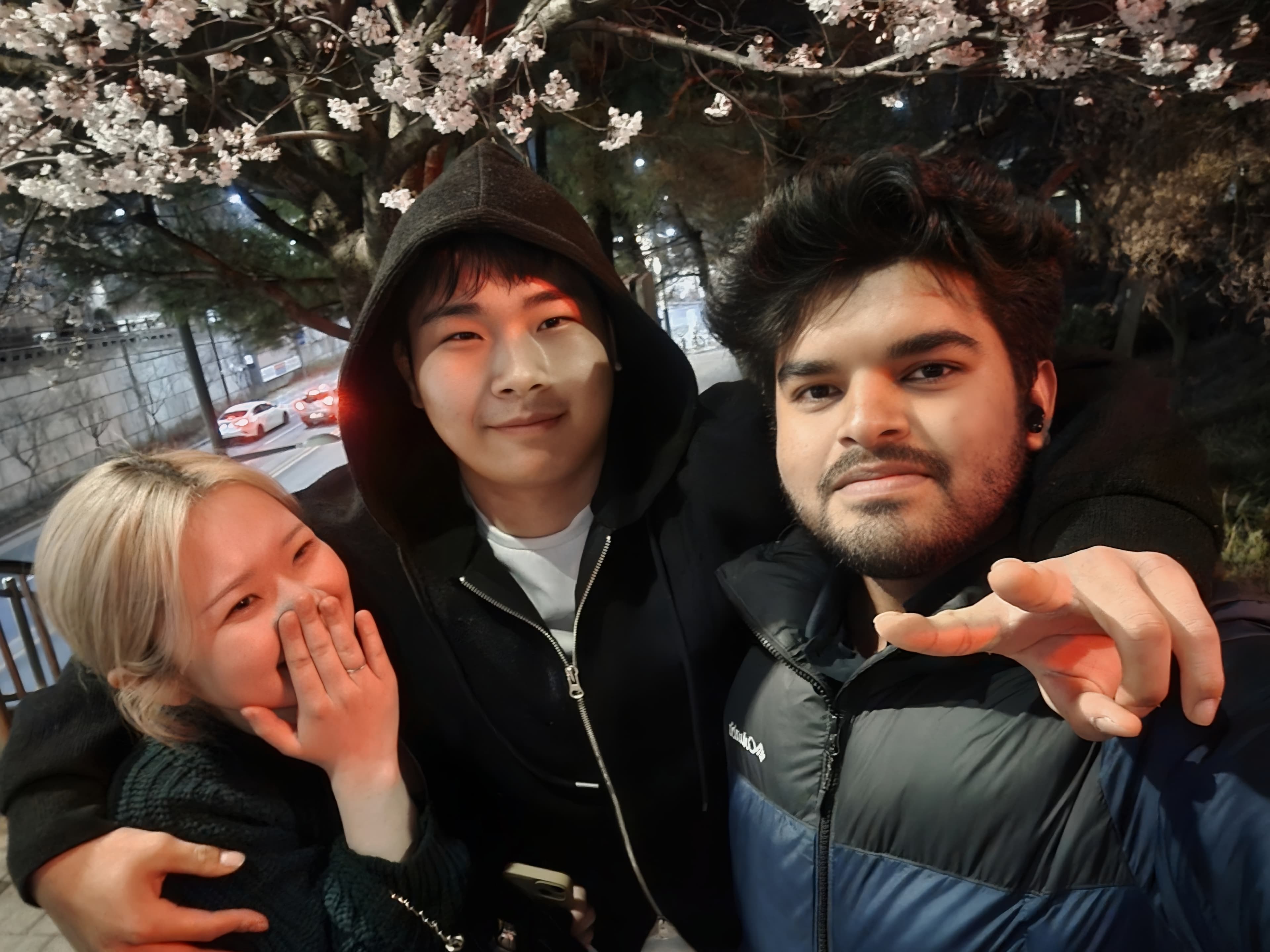 Shawkat Hossain Maruf taking a selfie with a friendly Korean couple under the cherry blossoms late at night during the spring season in Seoul.